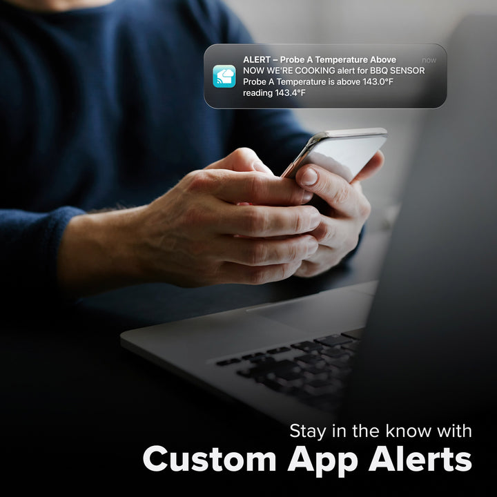 La Crosse Technology Alert and Monitoring system with a male sitting in front of a laptop receiving a message on their smartphone of an alert that their meat thermometer barbeque sensor temperature has  gone above the parameters of a custom alert for the bbq sensor with text that says stay in the know with Custom Alerts
