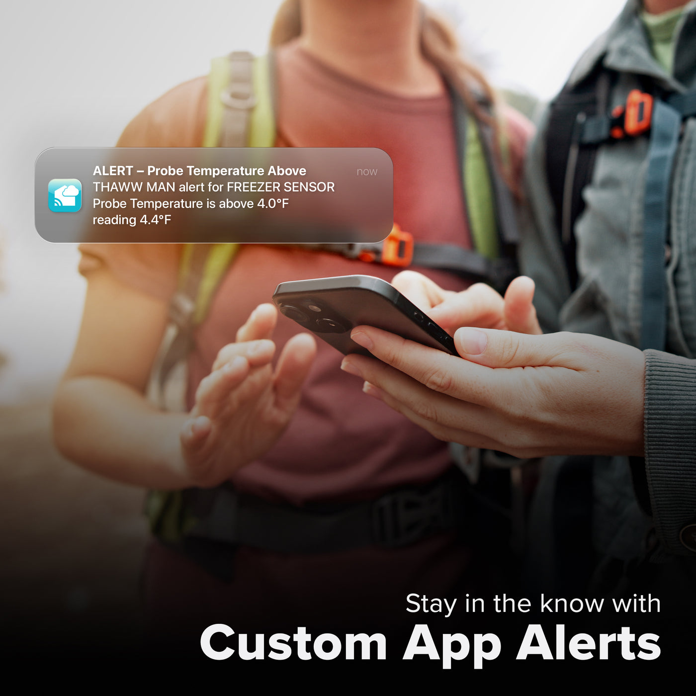 La Crosse Technology Alert and Monitoring system showing a female and male hiking looking at a smartphone receiving an alert for the  freezer temperature increasing outside of the parameters of the custom alert for a temperature probe sensor with text that says stay in the know with Custom Alerts