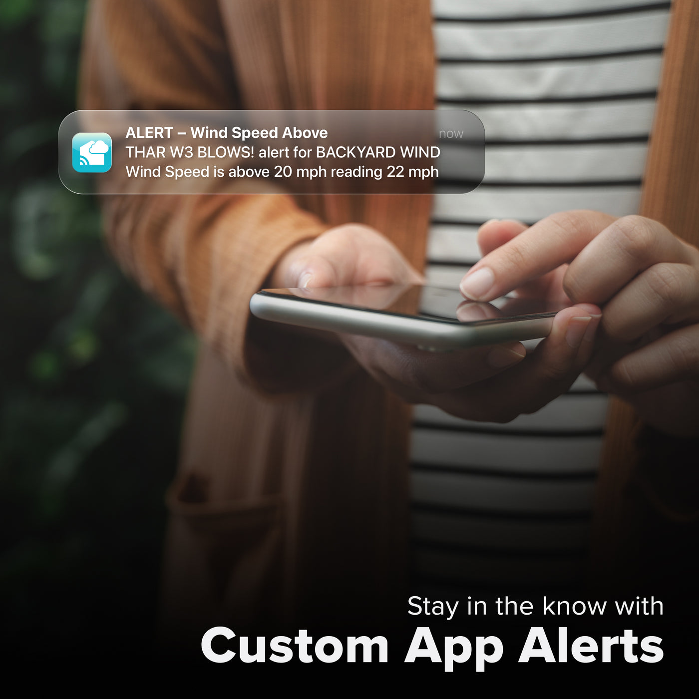 La Crosse Technology Alert and Monitoring system with someone looking at their smartphone receiving an alert for a wind sensor reaching speeds above the set parameters of a custom alert for the Glide wind speed sensor with text that says stay in the know with Custom Alerts