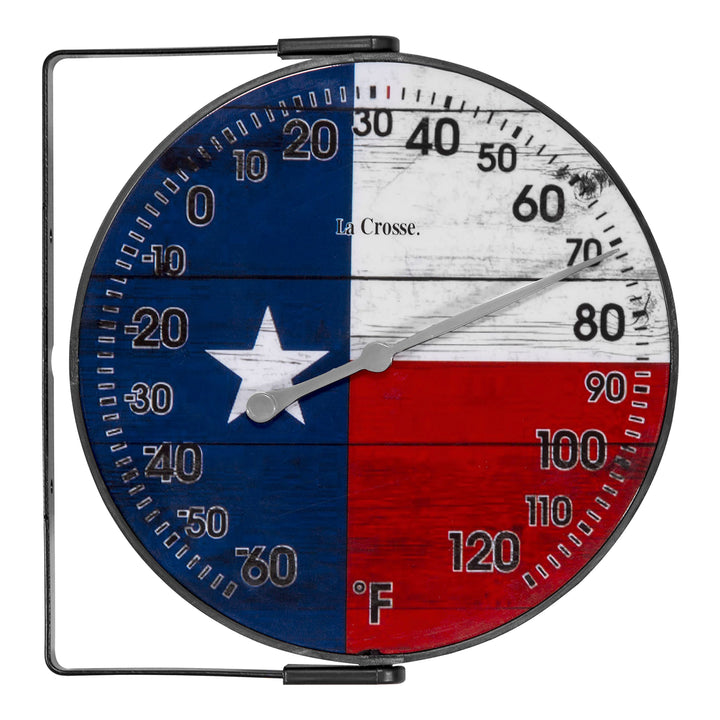 Head-on image of the 104-105TX 5-inch Dial Thermometer with Bracket that is positioned on the left side. The dial features black numbers on a rustic Americana flag in red, white, and blue with a white star, over rustic weathered boards, surrounded by a black frame with an adjustable bracket for mounting. Featuring a silver pointer that provides the temperature reading in Fahrenheit from -60-120 degrees.