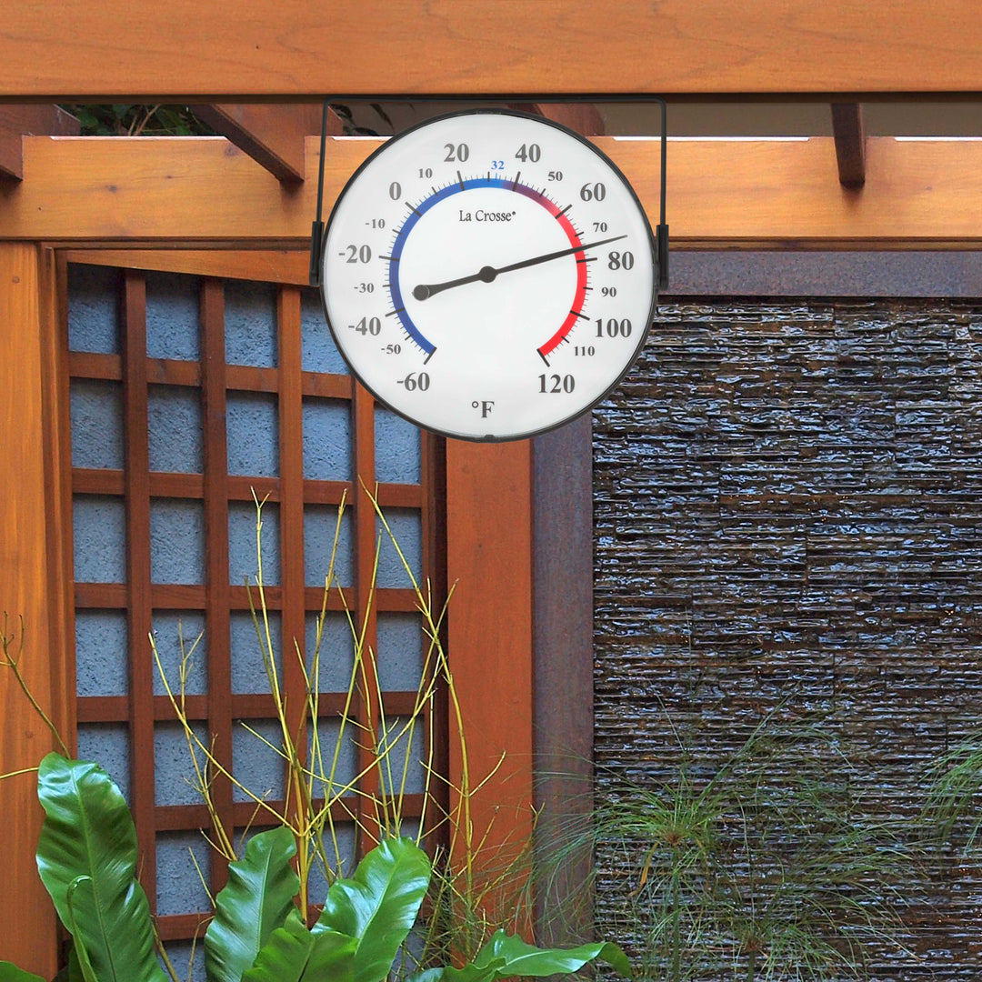104-105 5-inch Dial Thermometer with Bracket hanging from a pergola post, using the bracket in the top position. The bracket allows for four different mounting positions, or as a kickstand for table placement. The dial reads in degrees Fahrenheit from -60 to 120, with a color scale from blue (cold) to red (warm).