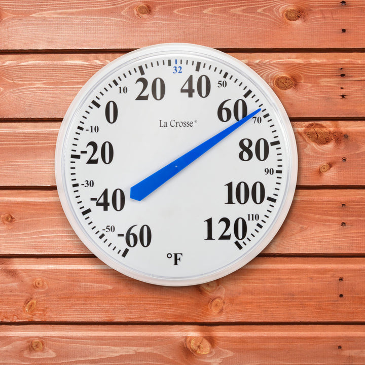 The 104-114A 13.5-inch dial thermometer with key hider, displaying the white dial with black numbers in degrees Fahrenheit from minus 60 to 120 degrees and a blue pointer highlighting freezing at 32 degrees shown hanging on a cedar color board wall or shed reading 67 degrees