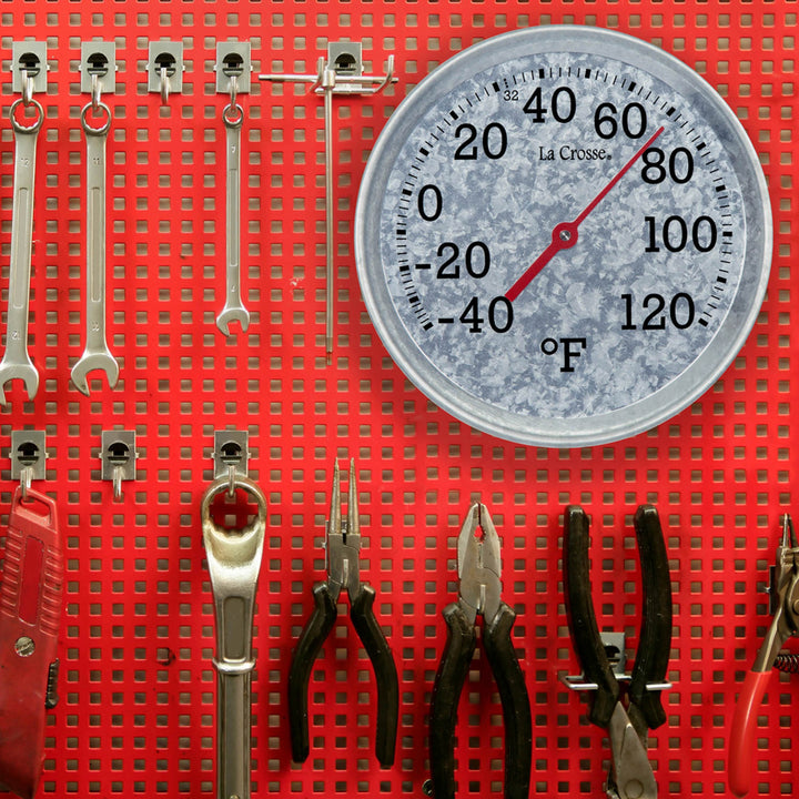 104-2822 8-inch Galvanized Dial Thermometer, galvanized metal dial with black number markings and a red pointer with a temperature scale from -40 to 120 degrees Fahrenheit hanging on a red pegboard wall with tools