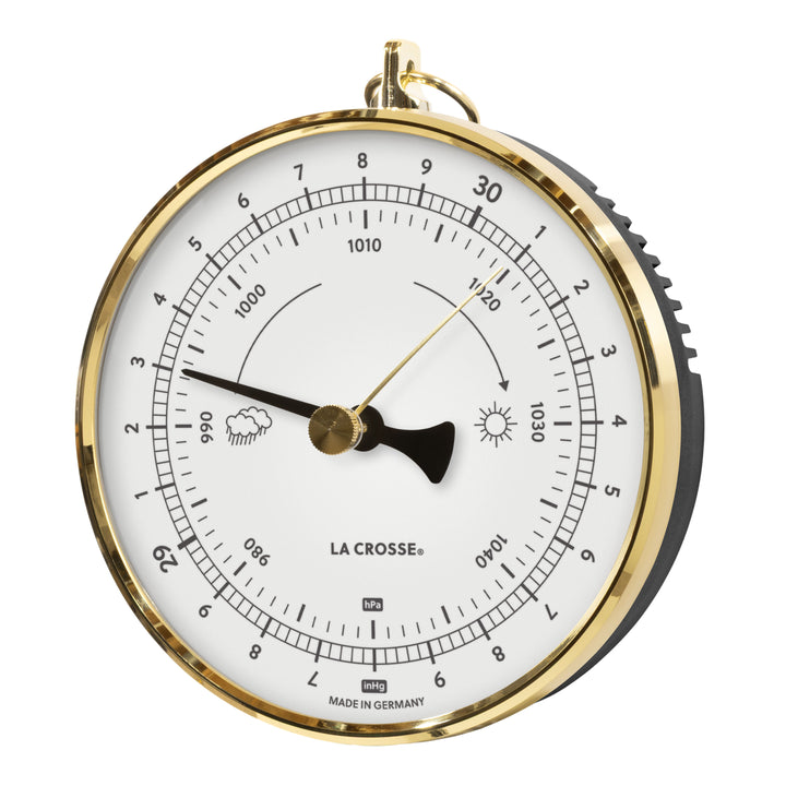 Left-facing image of the 138-1611W Analog Barometer - White featuring a brass case with a dome lens covering a white dial, brass reference marker, a black pressure indicator, black numbers, icons, and text. The barometer measures the atmospheric pressure in Hectopascals (hPa) and in Inches of Mercury (inHg) Made in Germany.
