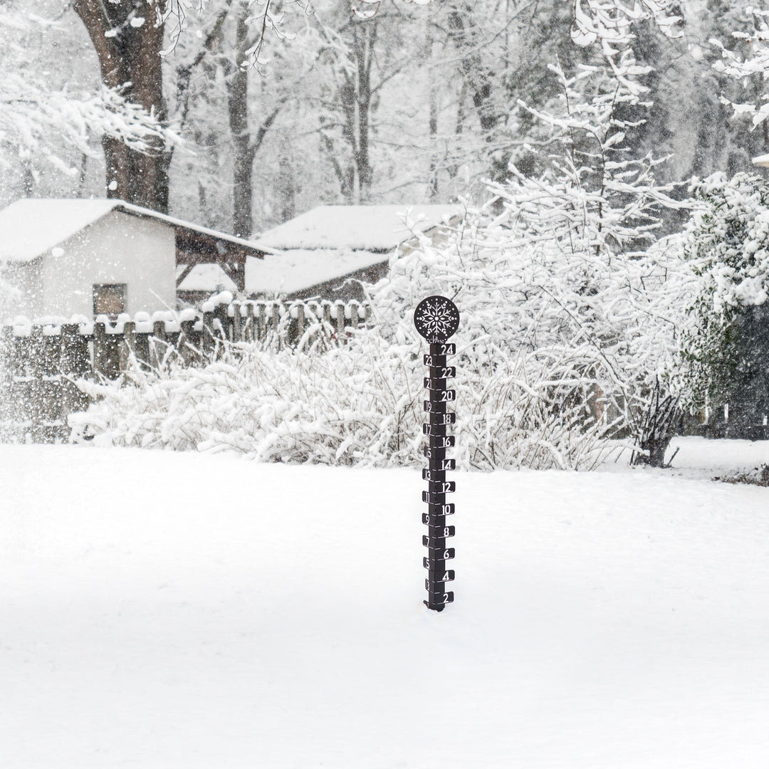 Lifstyle image of a snowy backyard with snow covered trrees, fencing, and house in the background with the 139-4686 Metal snowgague in the foreground