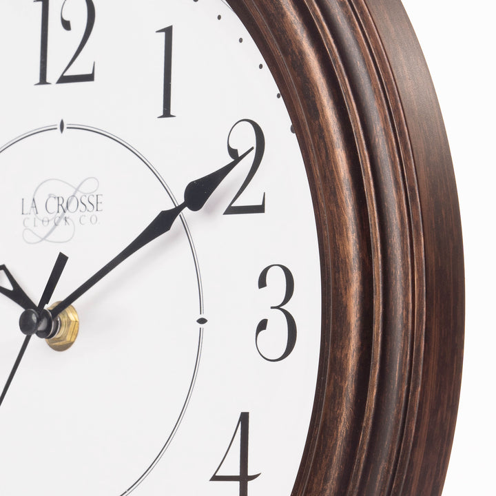 Close up view of the frame of the 404-2630W Evelyn analog wall clock showing the bronze finish, the stylized black numbers on a white dial