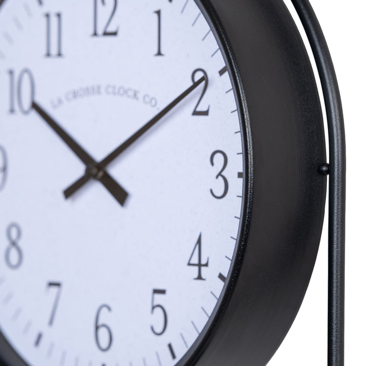 Close-up image of the metal frame of the 404-3022 Depot Wall Clock with Basket and Shelf featuring a Black Metal Frame, an archival paper-inspired dial, black numbers, and black metal hour and minute hands.
