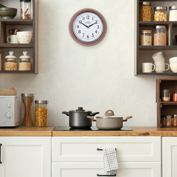 Lifestyle image of the 404-3024TC 9.5-inch Diner Clock – Terracotta shown hanging on a cream kitchen wall above a stove top and cabinets. The clock features a retro-style terracotta frame with a white dial, chrome bezel, black numbers and minute markings, black metal hands, and a silver second hand.