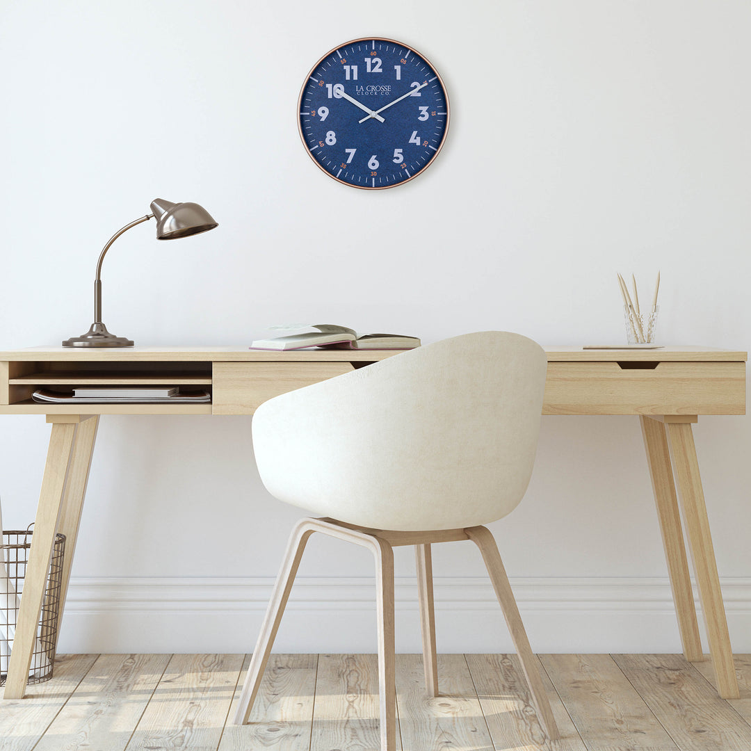 404-3027C Portside Navy blue eleven inch wall clock with white numbers copper time markings and a copper case and white hour and minute hands hanging on a wall over a Scandinavian style desk and chair with light wood flooring