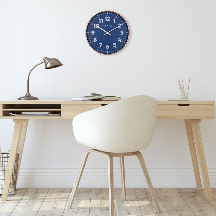 404-3027C Portside Navy blue eleven inch wall clock with white numbers copper time markings and a copper case and white hour and minute hands hanging on a wall over a Scandinavian style desk and chair with light wood flooring