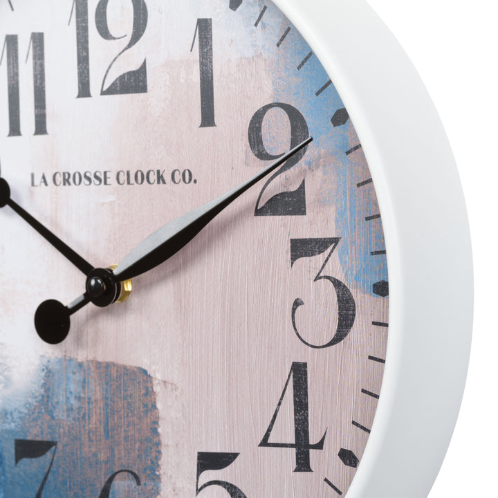 Close up image of the Brushstroke 404-3028A 11 inch wall clock highlighting the white case that surrounds a painted brush design dial in blues creams and taupe black with numbers and black metal hands