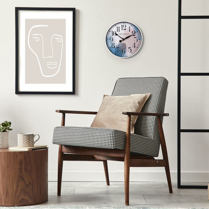 11 inch 404-3028A Brushstroke wall clock with a white case that surrounds a painted brush design dial in blues creams and taupe with black numbers and metal hands on a tan wall with modern art hanging above a houndstooth chair in black tans and creams