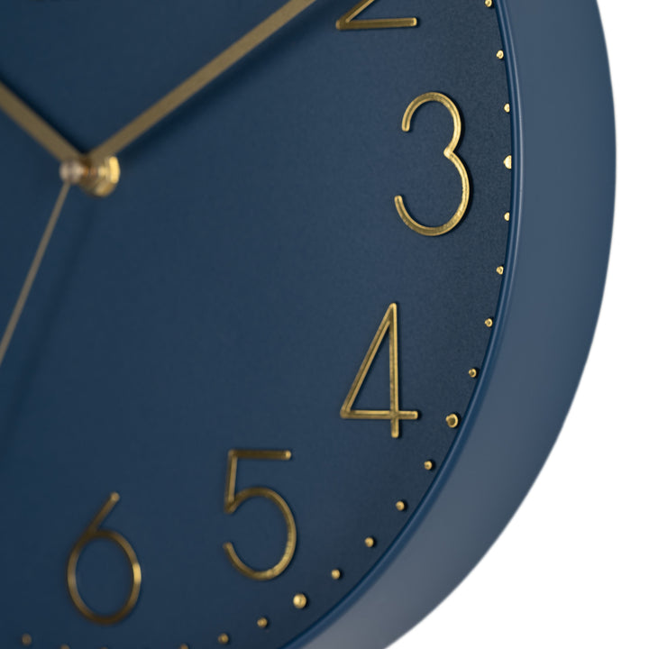 Close-up image highlighting the frame of the 404-3831NB 12-inch Paxton Wall Clock - Navy Blue, with Silent Sweep, featuring a flush-mount navy blue frame, a matching color dial, brass raised numbers, and brass-finished hour, minute, and second hands.