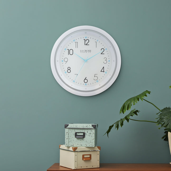 404-4525 white wall clock with blue hands shown in a daytime lifestyle on a green wall