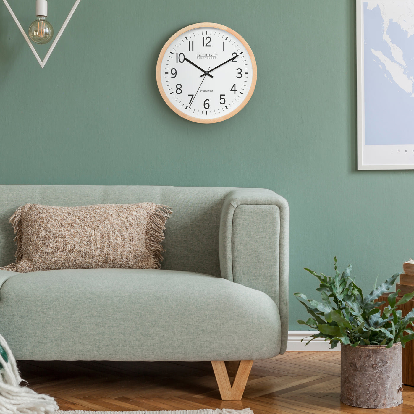 Wall clock on a green wall above a gray sofa with a plant in the corner.