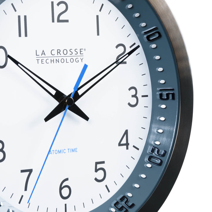 Close-up image of the dial of the 404-54667 10-inch Atomic Metal Wall Clock with Blue Chapter Ring. The clock features a black stainless steel frame with a blue chapter ring and raised seconds indicators, surrounding a white dial with black numbers, metal hands, and a blue accent second hand.