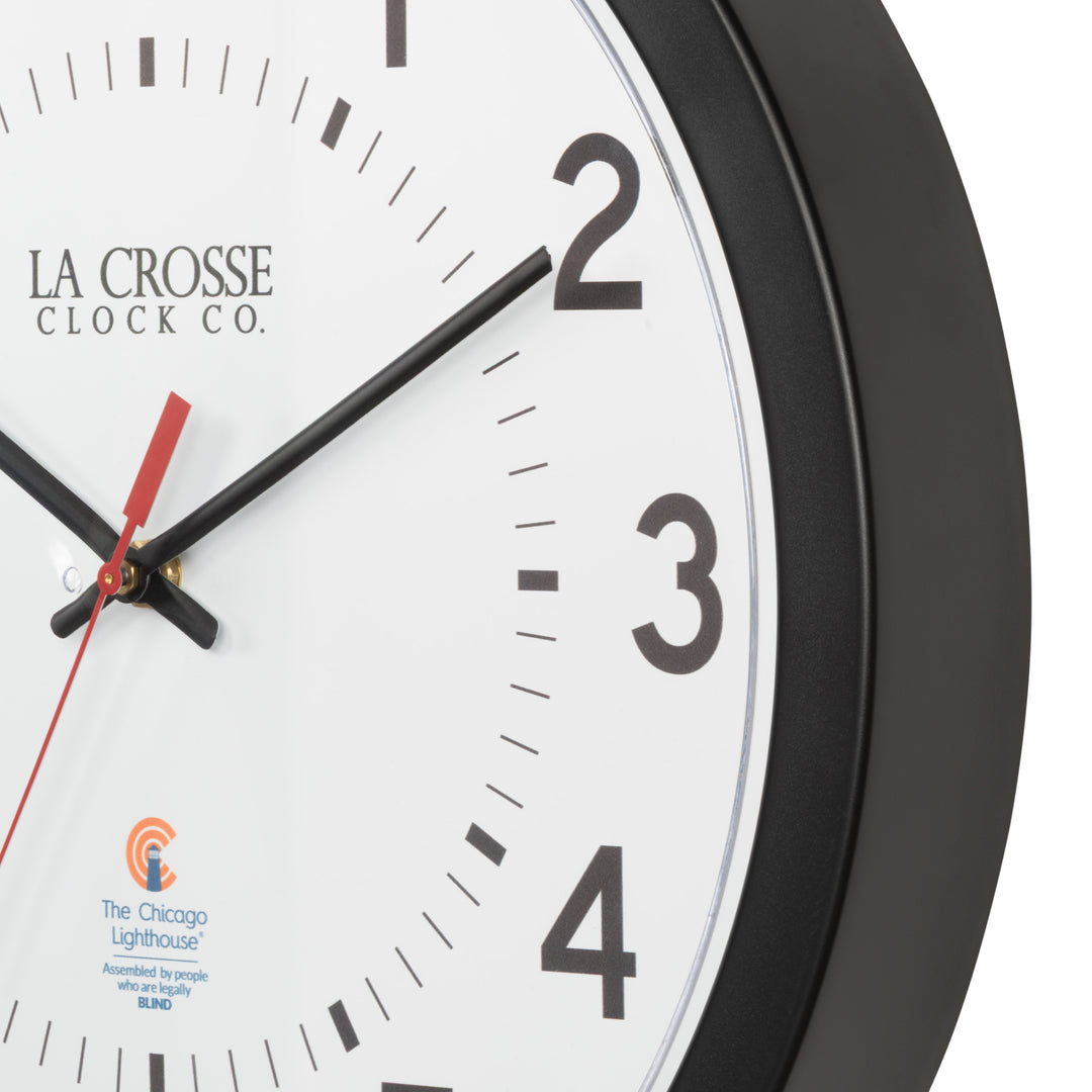 Frame closeup image of the 404-5537 14.5-inch Wall Clock  featuring a black flush mount frame, black bold numbers, black hour and minute hands, and a red second hand with two logos on the clock face, La Crosse Clock Co. and Chicago Lighthouse industries.