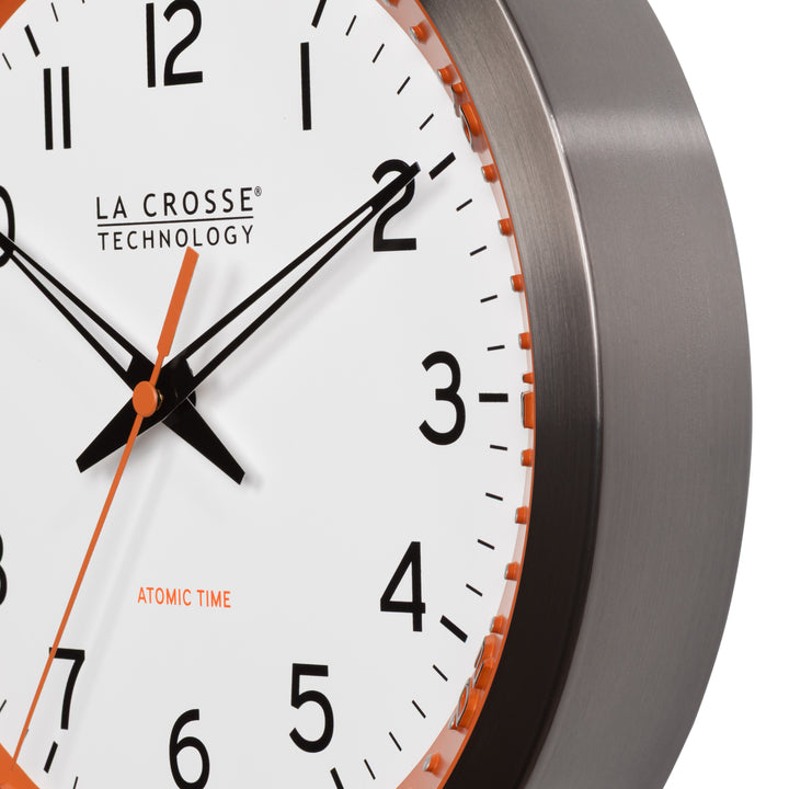 Frame close-up of the 404-87696 10-inch Atomic Metal Wall Clock - Chapter Ring: Orange. The clock features a white dial, an orange chapter ring with seconds indicator, black hands, an orange second hand, and a stainless steel flush-mount frame.