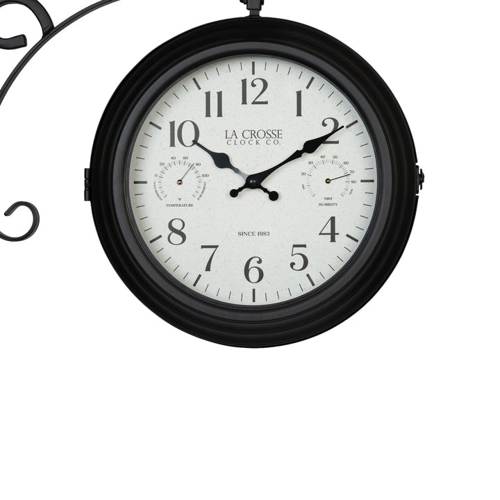 Clock close-up of the 425-34188 Outdoor Dual-Sided Metal Pedestal Clock. The clock features a temperature dial in a Fahrenheit scale, a humidity dial, decorative black metal hands, black numbers on a flecked white dial surrounded by a dark brown metal frame., with a 72-inch decorative scrollwork pedestal with a plant hanger.