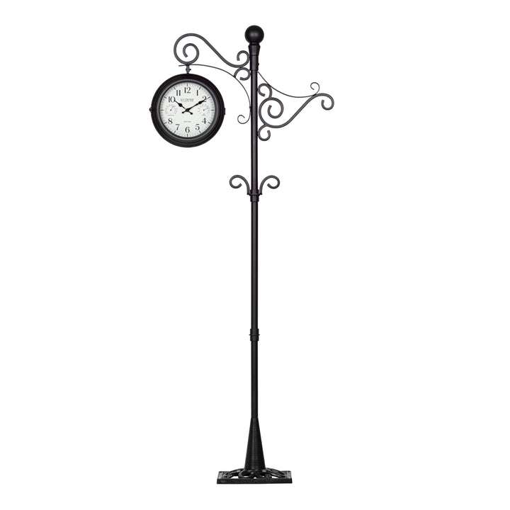 Full head-on image of the 425-34188 Outdoor Dual-Sided Metal Pedestal Clock. The clock features a temperature dial in a Fahrenheit scale, a humidity dial, decorative black metal hands, black numbers on a flecked white dial surrounded by a dark brown metal frame., with a 72-inch decorative scrollwork pedestal with a plant hanger.