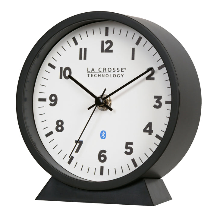 Left-facing image of the 437-3816 Insta-Set Table/Wall Clock with Bluetooth® Technology featuring a white dial with bold black numerals, black metal hands, and a black frame with removable base for tabletop or wall hanging placement.