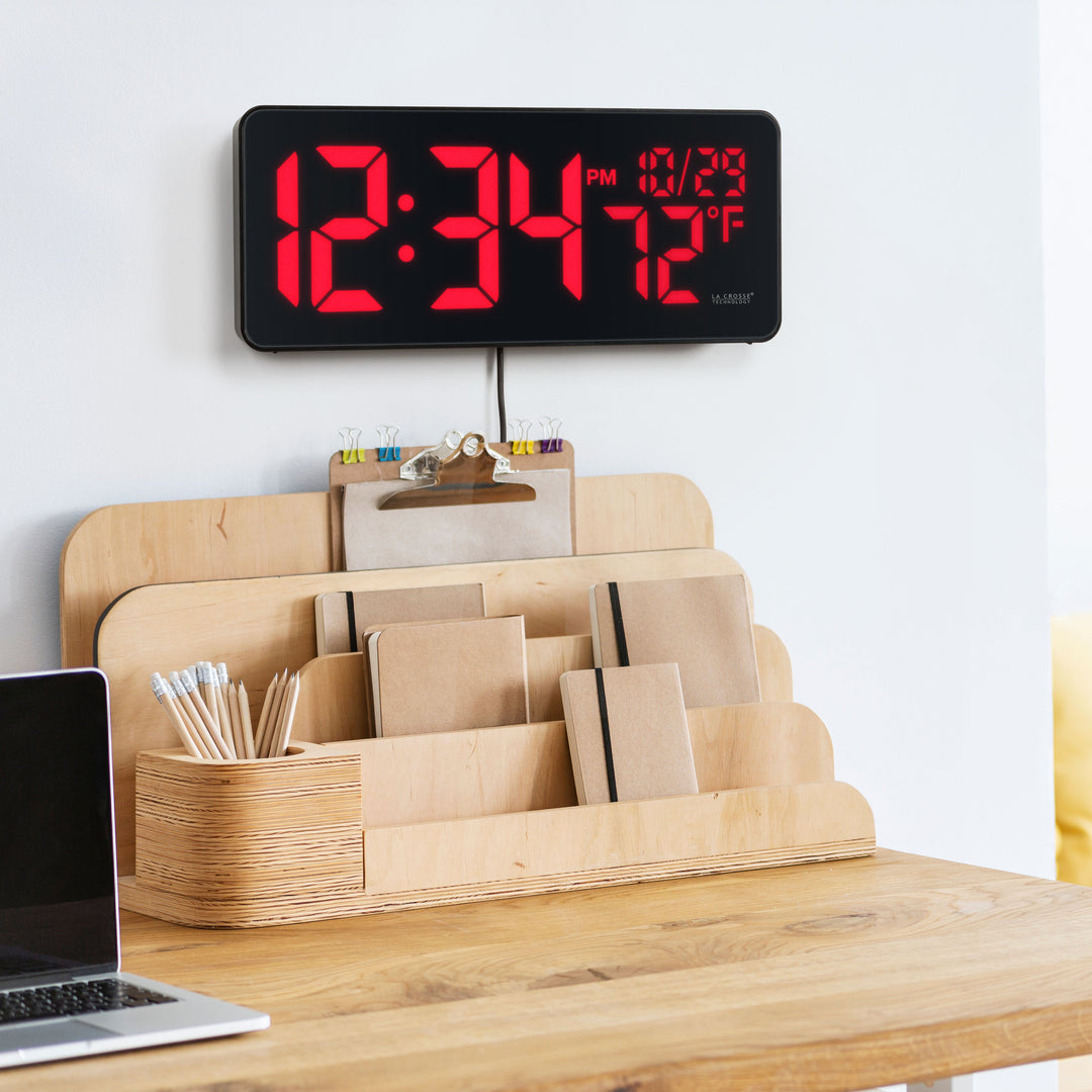 Lifestyle image of the 513-1411R Digital LED Wall Clock with Indoor Temperature hanging on a wall above a desk organizier. The digital wall clock features large 3-inch LED time digits, indoor temperature, and the date.