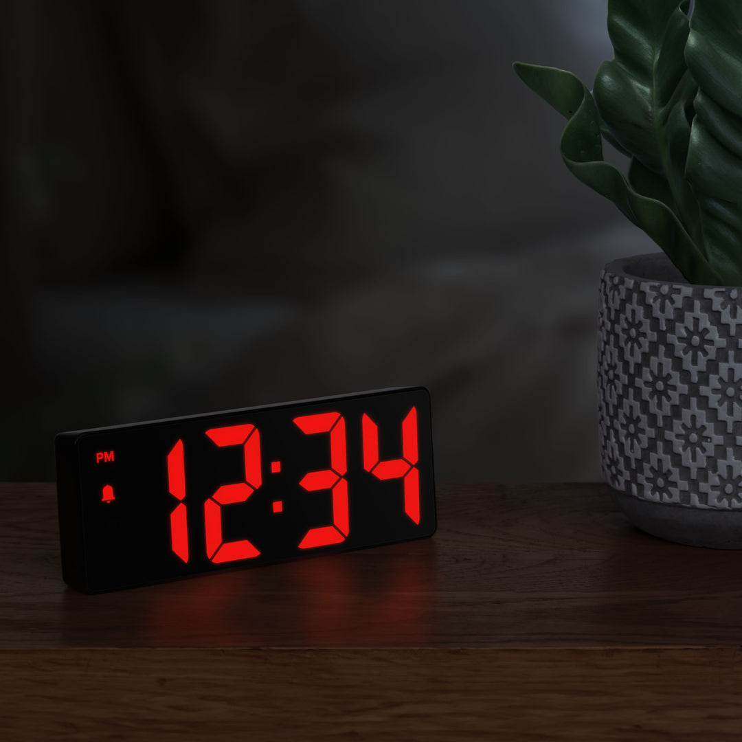 Lifestyle image of the 617-546 2.0-inch Red LED Alarm Clock with indoor temperature shown on a wood side table in a night scene. The clock reads 12:34pm and features 2-inch time digits, with alarm and PM indicators.