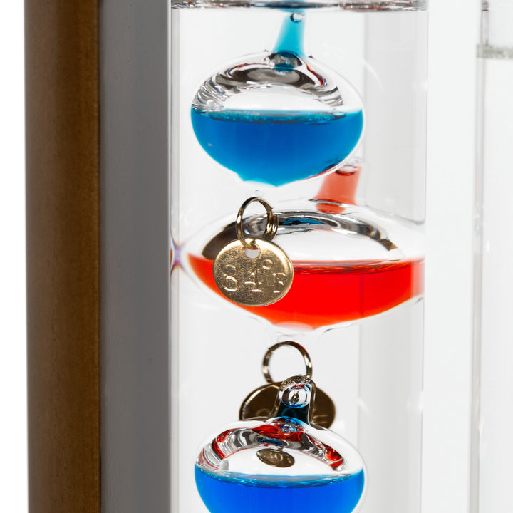 Close-up detail image of the 914-4928SG 11-inch Galileo Thermometer + FitzRoy Storm Glass showing the wood walnut finished casing and a glass tube with floating temperature spheres in various colors.