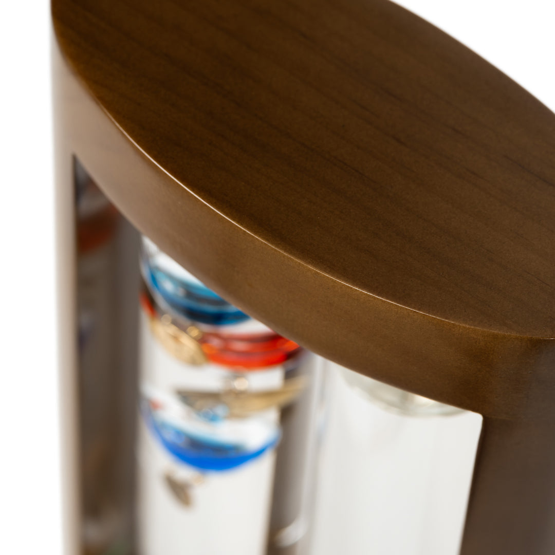 Close-up image of the casing fo the 914-4928SG 11-inch Galileo Thermometer + FitzRoy Storm Glass. The thermometer features a solid walnut-finished wooden casing with two glass tubes: one with floating temperature spheres in various colors, and the second containing a changing liquid that indicates the forecast.