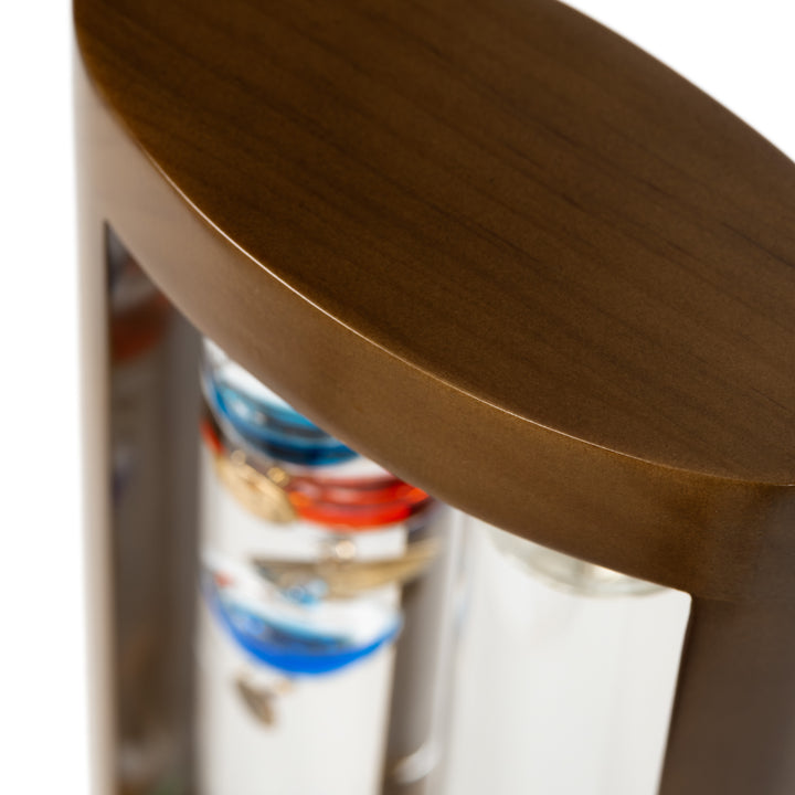 Close-up image of the casing fo the 914-4928SG 11-inch Galileo Thermometer + FitzRoy Storm Glass. The thermometer features a solid walnut-finished wooden casing with two glass tubes: one with floating temperature spheres in various colors, and the second containing a changing liquid that indicates the forecast.