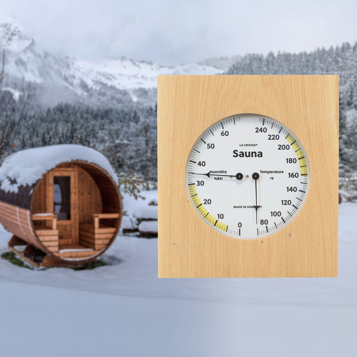 914-620 Sauna Thermometer and Hygrometer dial in oiled oak wood casing displaying a dial split in half with temperature on the right in Fahrenheit from 60 degrees to 245 degrees with optimal range in yellow and the left half showing humidity readings from 0 percent to 75 percent with the optimal range highlighted in yellow superimposed to the right over a lifestyle image of an outdoor Sauna in winter