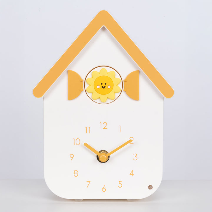 Head on image of W70063, a white house shaped clock with a smiley sun cuckoo with yellow numbers, shutters, roof, and hands