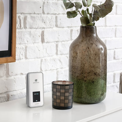 White and gray La Crosse Technology alert and monitoring system Bridge gateway on a white modern table with a vase and candle holder in fron of a white painted brick wall